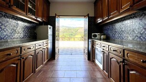 Une cuisine avec des meubles en bois, un réfrigérateur et un four à micro-ondes. On peut admirer, depuis la cuisine, un balcon dont le sol est carrelé et qui est accessible par une porte donnant sur l’extérieur.