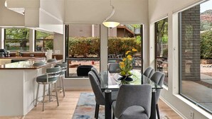 Une cuisine moderne avec un coin repas, de grandes fenêtres et une vue sur un jardin aménagé.
