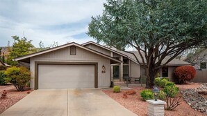 Une maison de plain-pied avec un garage, un grand arbre à l’avant et un jardin bien entretenu.