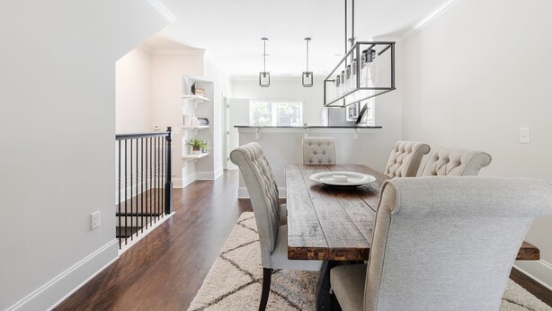 A modern dining area with a wooden table, upholstered chairs, and pendant lighting.