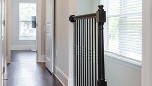 A hallway with a dark wooden floor, white walls, and a black railing with vertical bars.