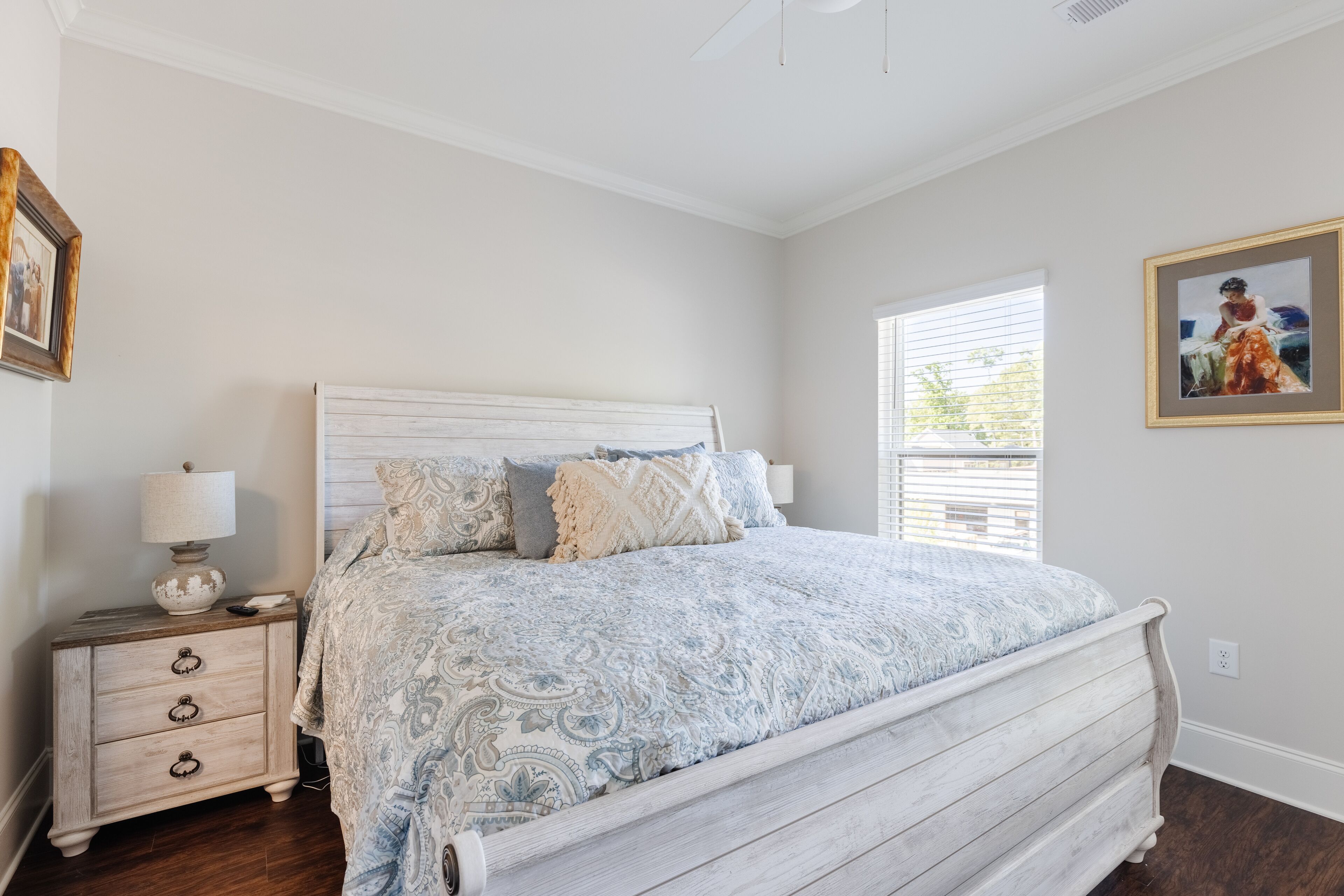 A bedroom with a bed, nightstand, lamp, and framed artwork on the wall.