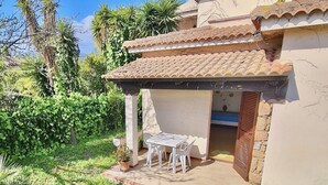 A house with a tiled roof, a patio with a table and chairs, and a garden with various plants. - Sa Chessa House Two-room apartment in San Teodoro (San Teodoro)