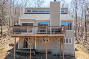 A two-story house with a deck, large windows, and a chimney.