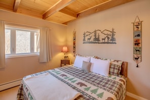 A bedroom with a bed, a window with curtains, a wall-mounted lamp, and a wall decoration of animals and trees.