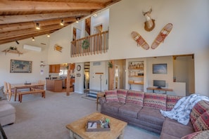 A spacious living area with a high ceiling, a cozy couch, a wooden coffee table, and a kitchen in the background.