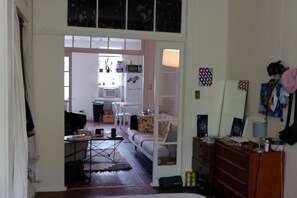 A room with a bed, a dresser, a desk, and a chair. There is a window with blinds, a door, and a small table with a plant. - 1 Bedroom Apartment in Brooklyn (Brooklyn)