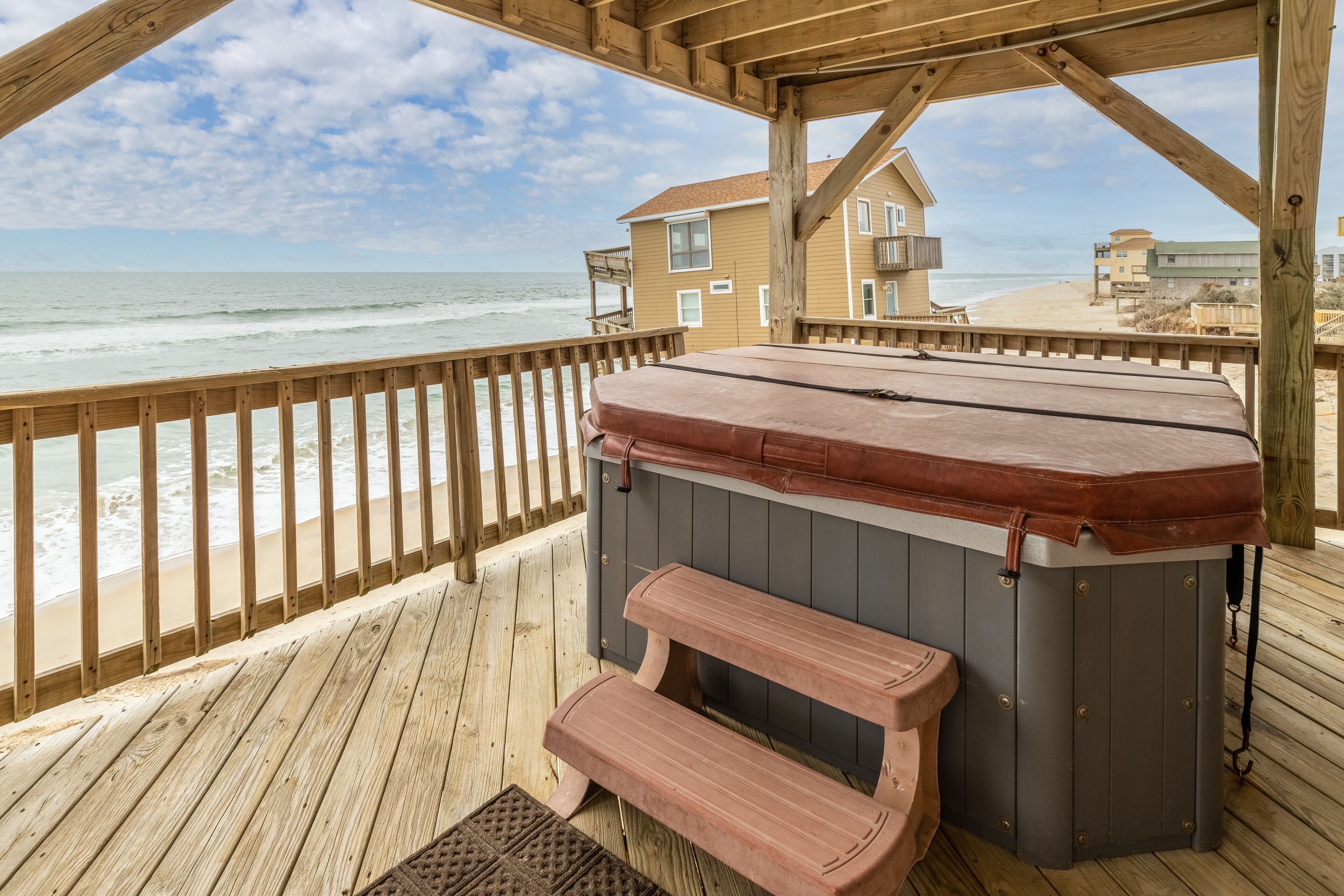 A wooden deck with a hot tub and bench overlooking a beach.