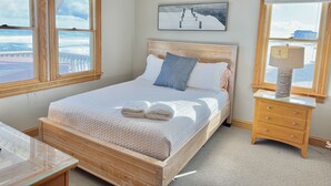 Un dormitorio con cama, mesita de noche y vistas al océano a través de amplios ventanales.