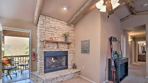 A stone fireplace with a fire, a wooden shelf above it, and a door leading to an outdoor area with a deck and chairs.