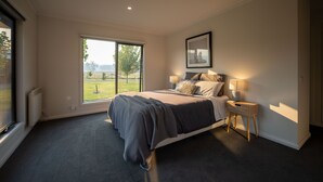 A modern bedroom with a large window, a bed with a grey duvet, two bedside tables with lamps, and a framed picture on the wall.