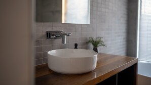 A modern bathroom with a round white sink, a wooden countertop, and a mirror above it.