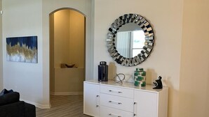 Een moderne woonkamer met een witte console tafel, een ronde spiegel en een schilderij aan de muur.