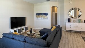 Een moderne woonkamer met een flatscreen-tv, een plafondventilator, een bank, een salontafel en een decoratieve spiegel.
