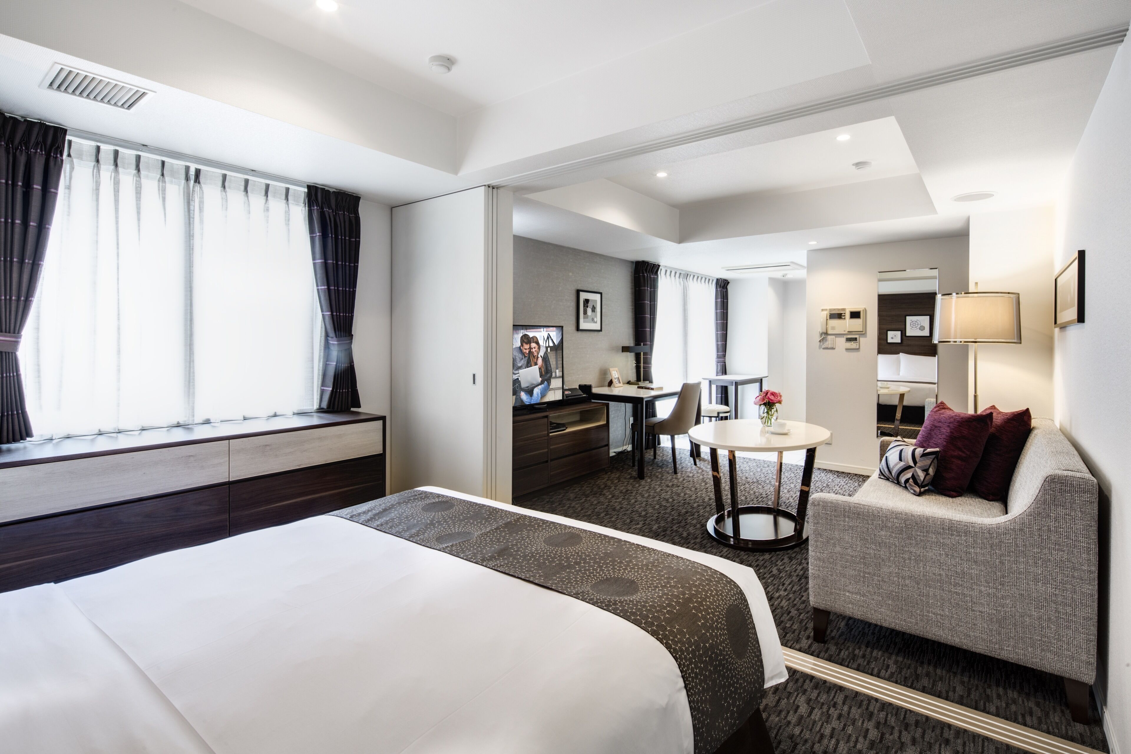 Quarto de hotel com cama, sofá, escrivaninha e uma pequena mesa.