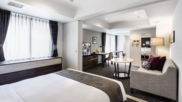 Quarto de hotel com cama, sofá, escrivaninha e uma pequena mesa.