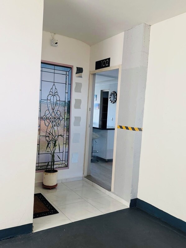 Un pasillo con una planta en maceta, una puerta con panel de vidrio y un reloj en la pared.