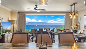 A dining area with a view of the ocean, a ceiling fan, and a TV on the left. - Maui Resort Rentals: Honua Kai Konea 929 – 9th Floor 3BR W/ Stunning Ocean Views from All 3 Bedrooms! (Lahaina)