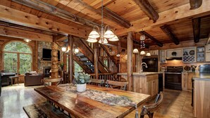 Un intérieur rustique en bois, avec une grande table à manger, une cheminée en pierre et un escalier menant à un étage supérieur.