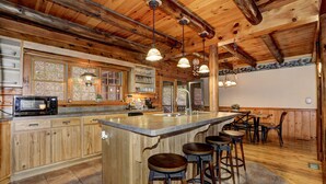 Une cuisine spacieuse avec des meubles en bois, un grand îlot central doté de tabourets et un éclairage suspendu.