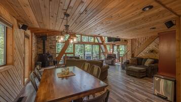 A spacious wooden cabin with a dining area, sofas, and a fireplace.