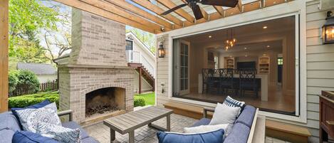 An outdoor patio with a brick fireplace, wooden furniture, and a ceiling fan.