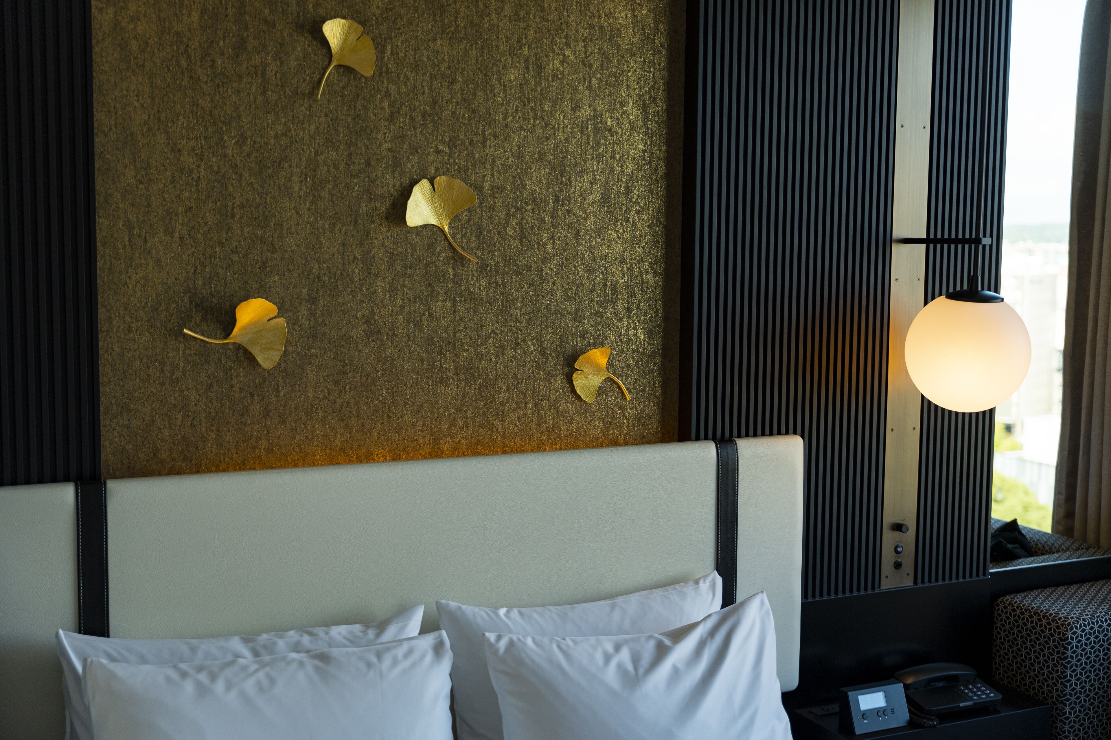 Habitación de hotel con una cama, una mesita de noche con teléfono y una pared decorada con hojas.