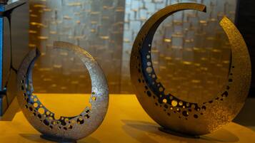Two metallic crescent sculptures with holes, placed on a table against a patterned wall.