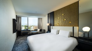 A hotel room with a large bed, a desk, a chair, a small table, and a large window offering a city view. - KOKO HOTEL Premier Kumamoto (Kumamoto)