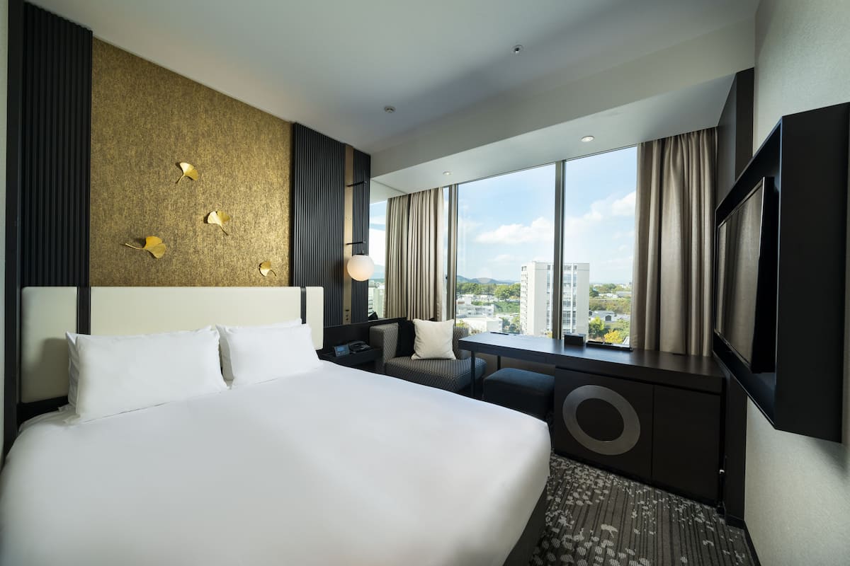 Een moderne hotelkamer met een groot bed, een bureau en uitzicht op de stad.