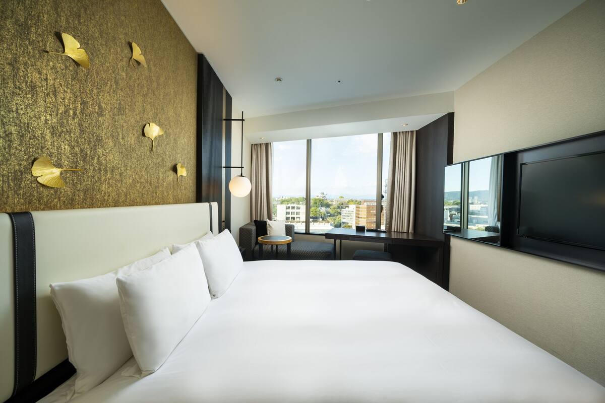 Een hotelkamer met een groot bed, een televisie, een bureau en uitzicht op de stad.