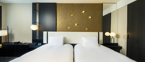 A hotel room with two beds, a large mirror, and a wall-mounted light fixture.