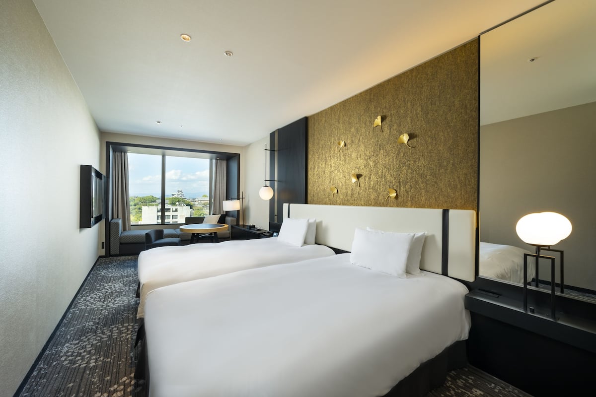 Een hotelkamer met twee bedden, een groot raam, een ronde tafel en een spiegel aan de muur.