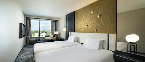 A hotel room with two beds, a large window, a round table, and a wall-mounted mirror.