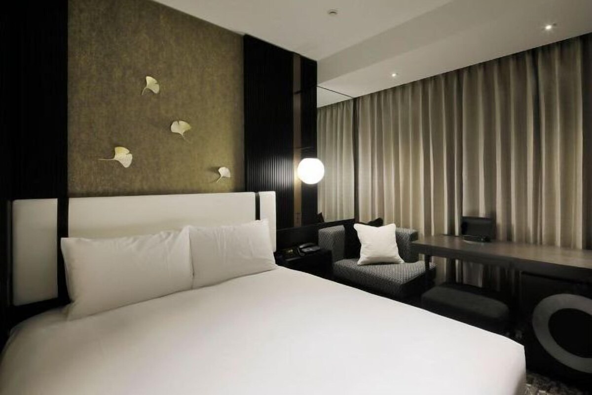 A modern hotel room with a large bed, a desk, and a view of the city.