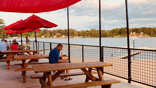 Outdoor picnic tables with red umbrellas, a lake view, and a fence.
