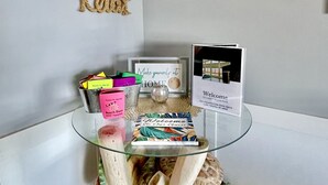 A glass table with a welcome card, a framed picture of a pier, and a wall-mounted mirror.