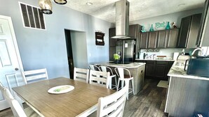 A modern kitchen with a central island, white chairs, and a wooden dining table.