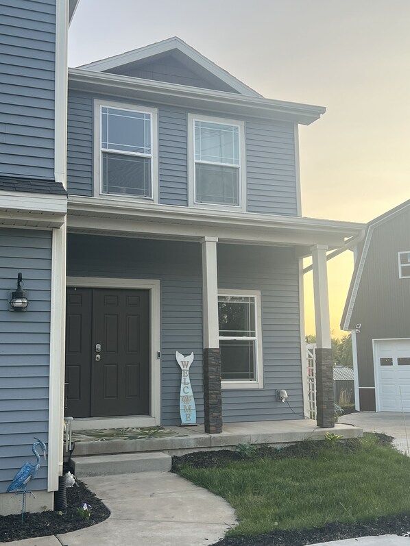 A two-story house with a dark front door, a welcome sign, and a bird sculpture in the front yard.