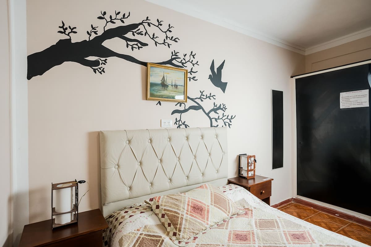 Une chambre à coucher comprenant un lit, une table de chevet, un tableau encadré et un motif décoratif représentant un arbre et un navire.