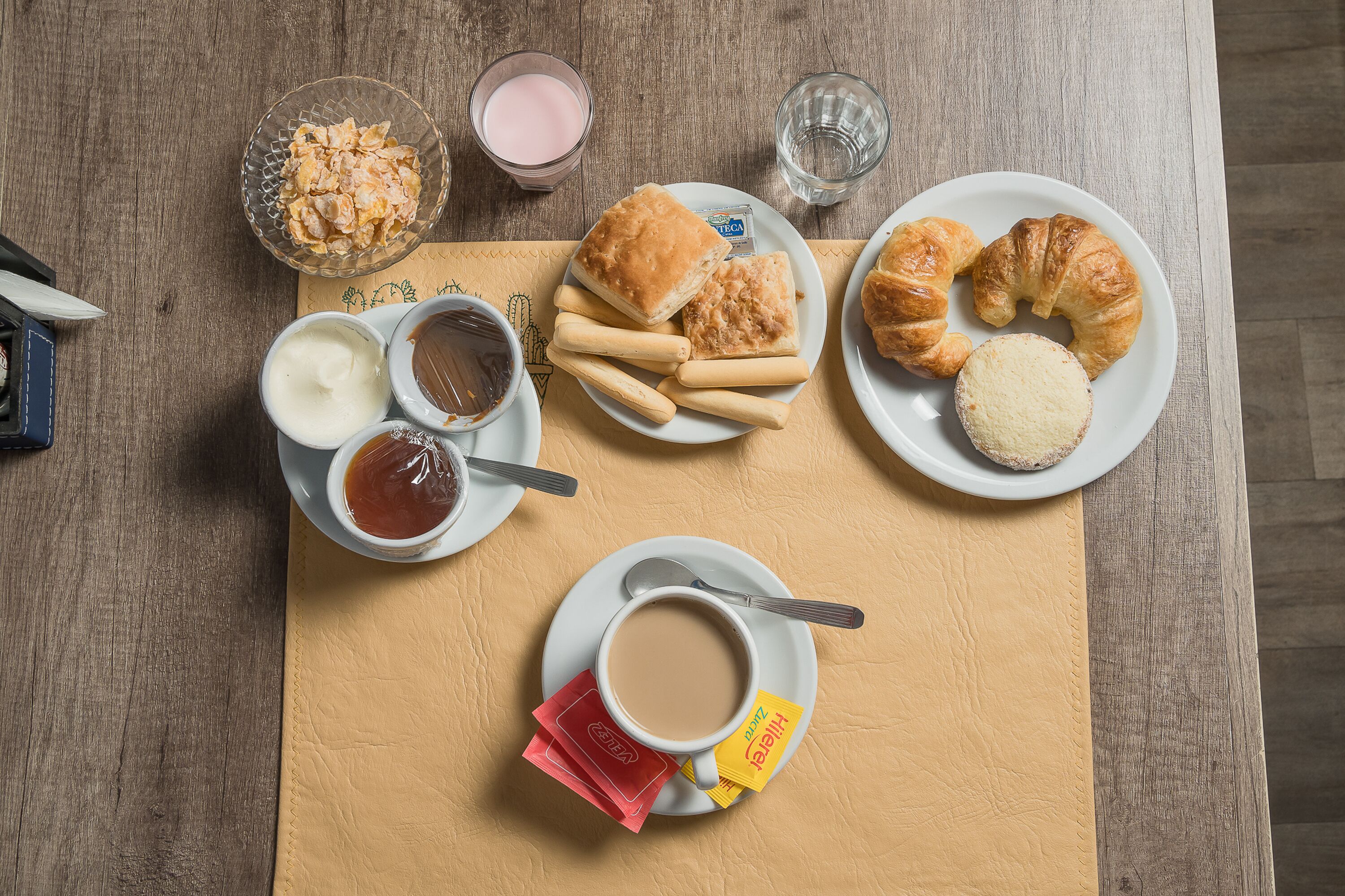 Desayuno con cruasanes, muffins y una taza de café sobre una mesa de madera.