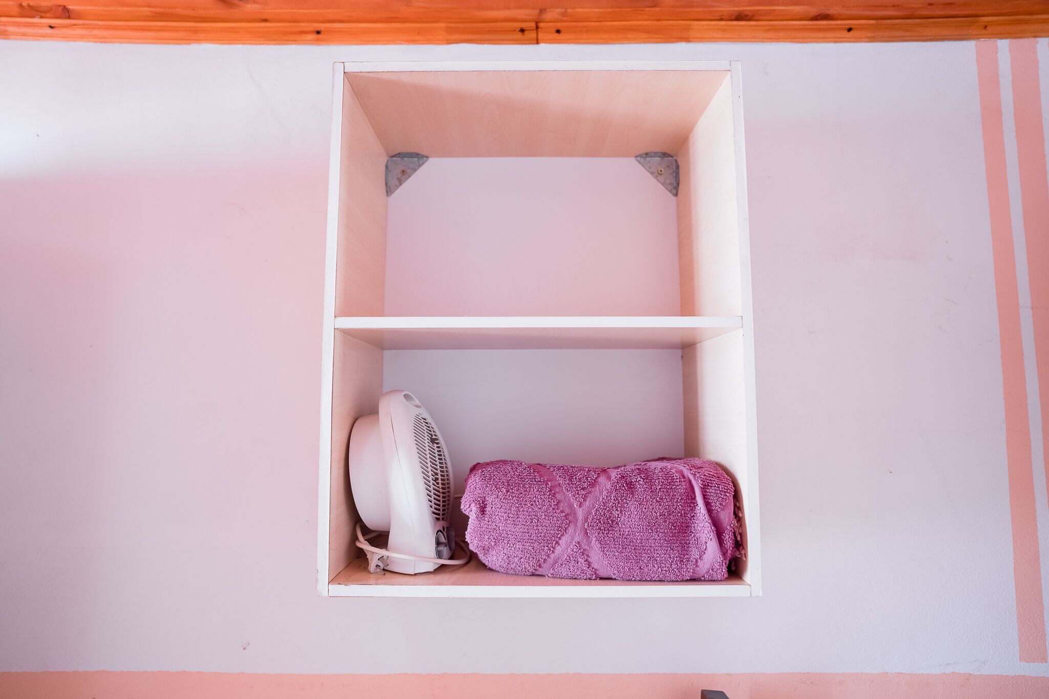 A small, empty white shelf unit with a fan and a rolled-up towel.