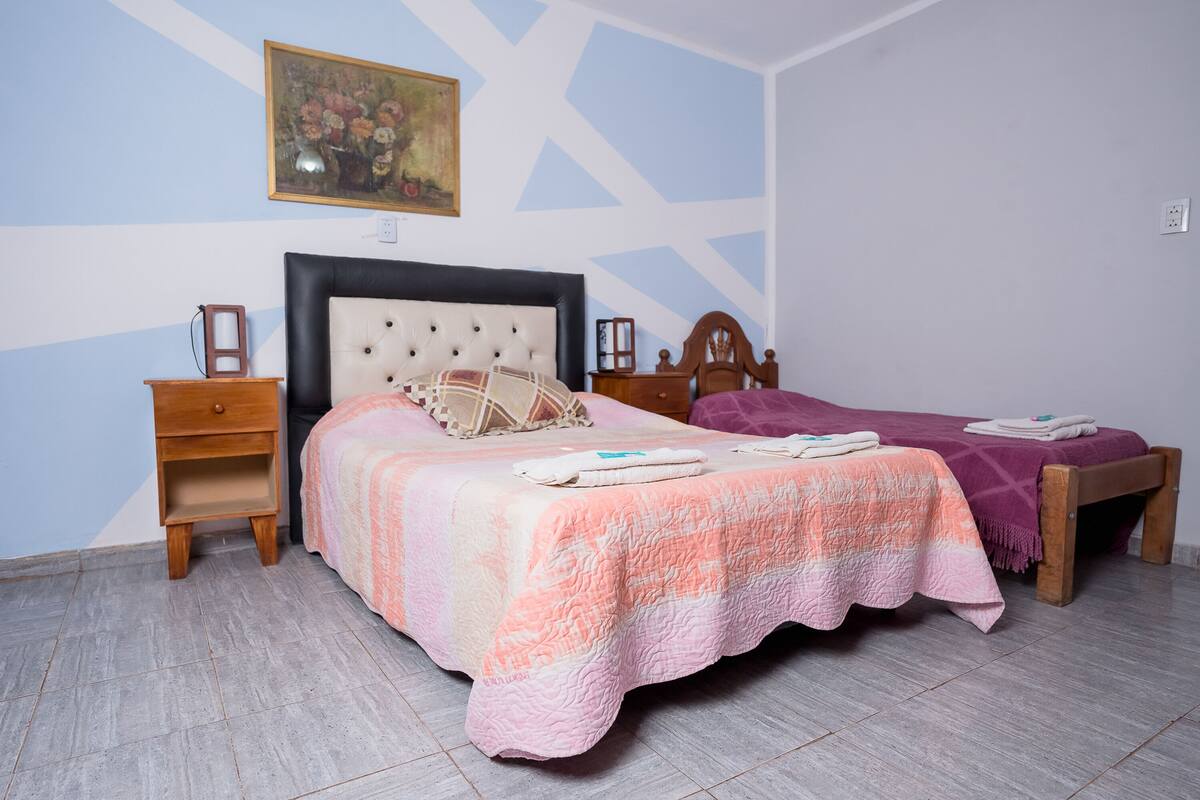 Une chambre à coucher avec un lit, deux tables de chevet, une chaise en bois et un tableau accroché au mur.