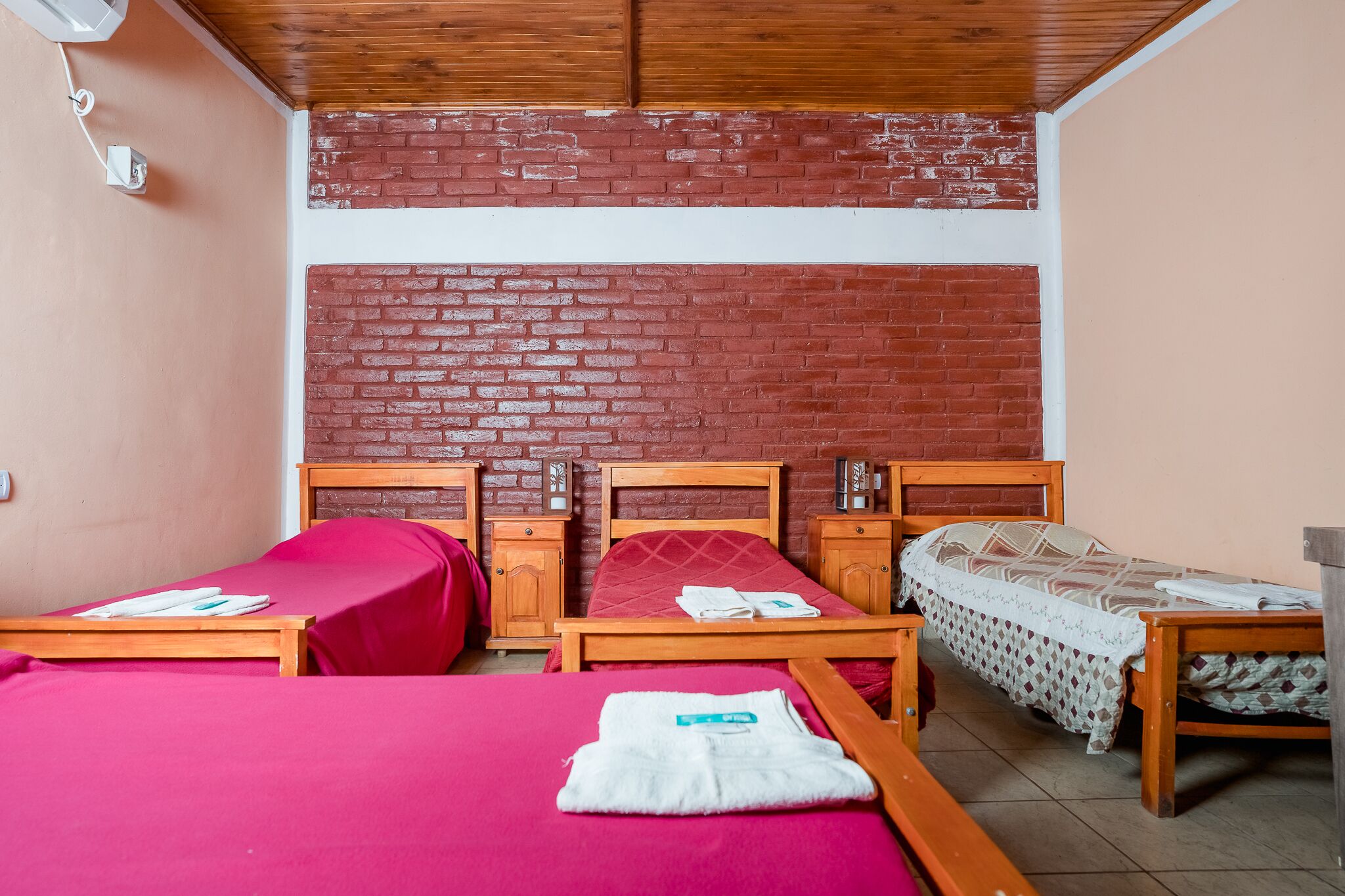 A room with two beds, a brick wall, wooden furniture, and a small table.