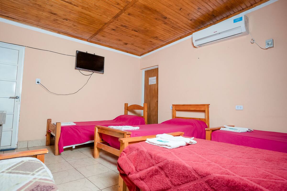 Une chambre avec deux lits en bois, un téléviseur fixé au mur et un appareil de climatisation.
