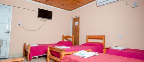 A room with two wooden beds, a television mounted on the wall, and an air conditioning unit.