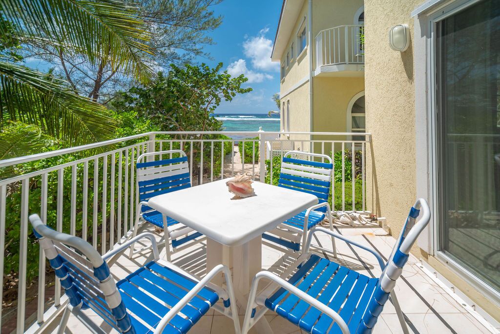 A balcony with a table and chairs, overlooking the ocean.
