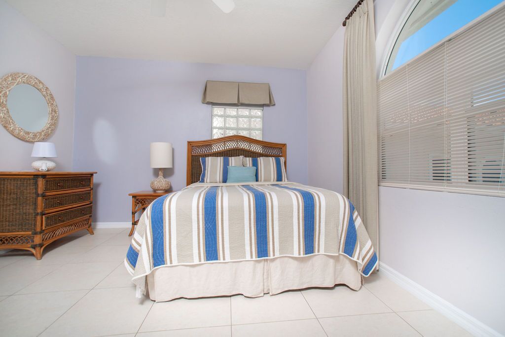 Une chambre à coucher comprenant un lit, une commode, un miroir et une fenêtre avec des stores.