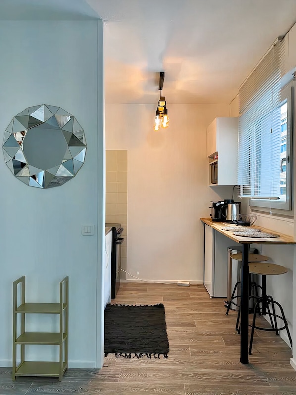 Uma cozinha moderna com piso de madeira, um espelho redondo, luminária pendente e janela com persianas.