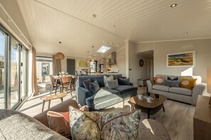 A spacious living area with a high ceiling, large windows, and a dining area.